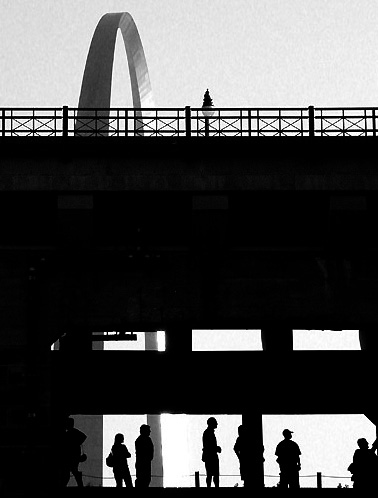people waiting for the train silhouetted against Arch