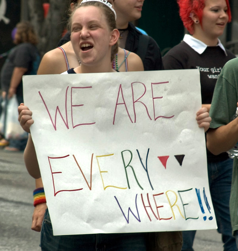 Young woman, joyful smile, wearing a tiara and carrying a homemade sign that says, "WE ARE EVERYWHERE" in rainbow colors. At the Pride Parade in St. Louis, 2005.